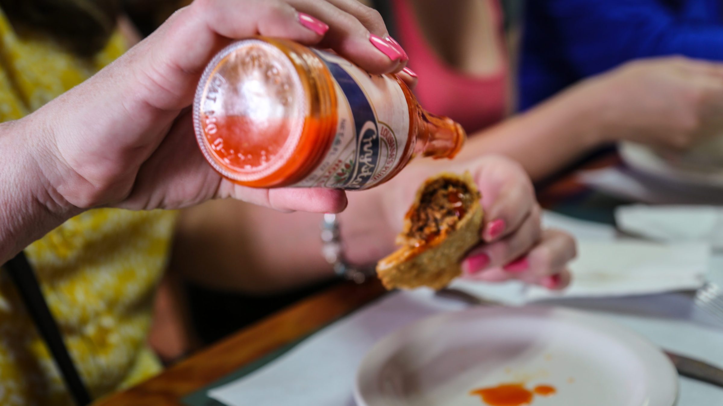 woman pouring hot sauce on empanada