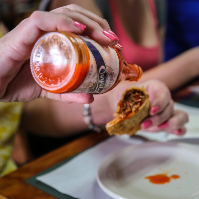 woman pouring hot sauce on empanada